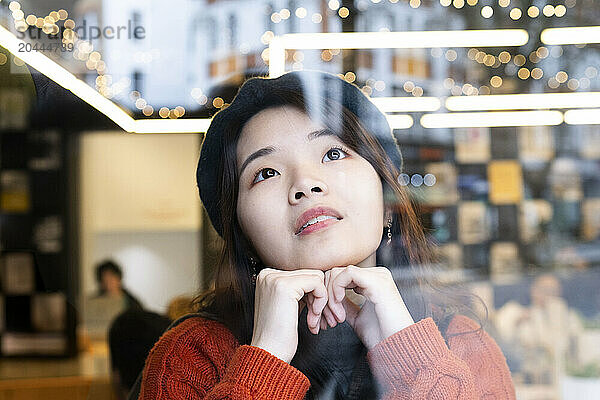 Beautiful young woman day dreaming seen through window glass