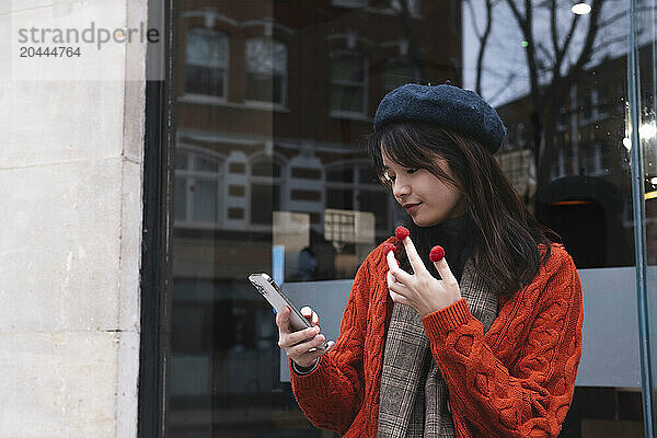 Young beautiful woman eating raspberry using smart phone