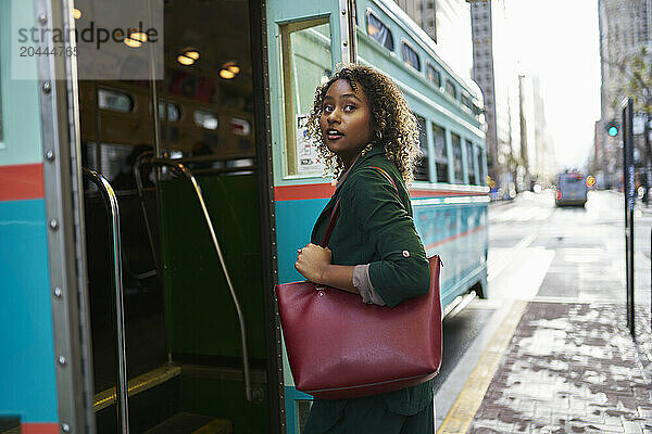 Beautiful young businesswoman with purse boarding bus in city