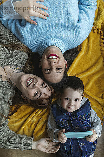 Happy women lying down with boy holding smart phone at home