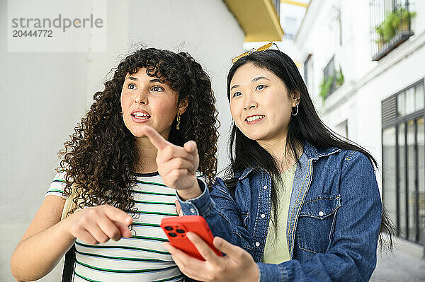 Young woman holding smartphone and standing next to friend