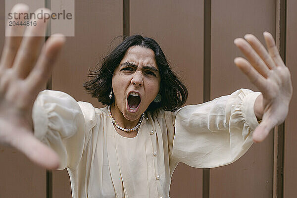 Woman showing stop gesture and screaming in front of wall