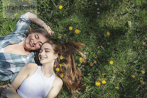 Happy mother and daughter lying on grass with dandelions in park