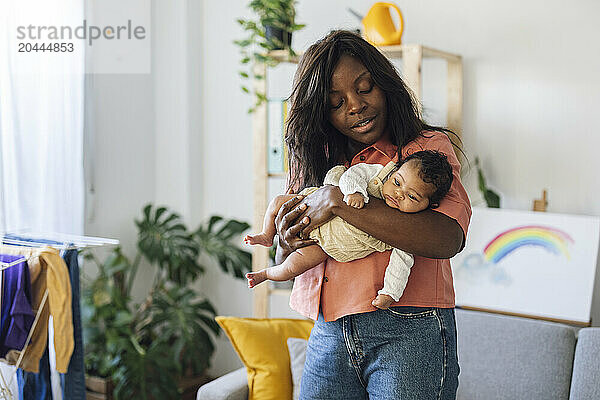 Mother holding daughter and standing in living room at home