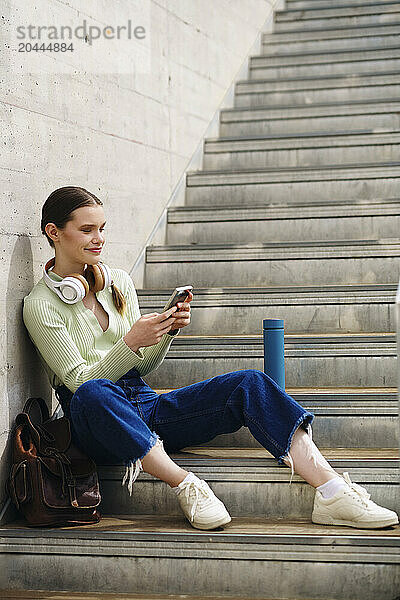 Smiling woman sitting on staircase and using smartphone