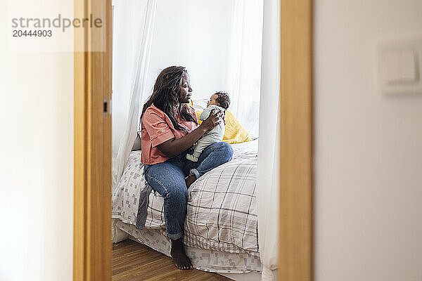 Mother holding daughter and sitting on bed in bedroom at home