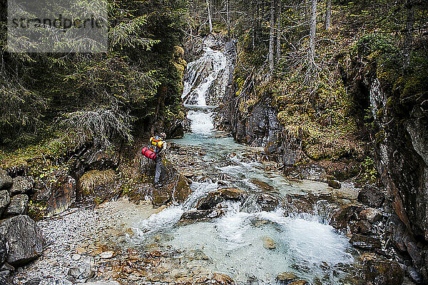 Senior man standing on rock near waterfall in forest