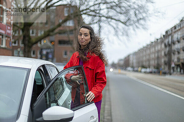 Young woman opening car door standing at street