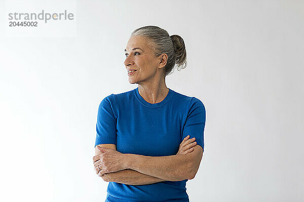 Senior woman with arms crossed in front of wall