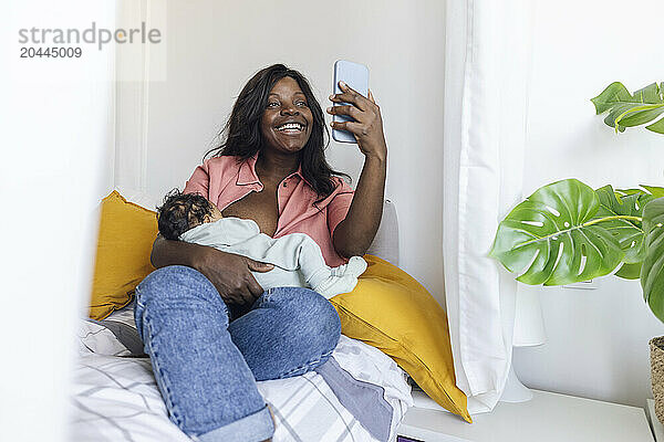 Happy mother breastfeeding and taking selfie at home