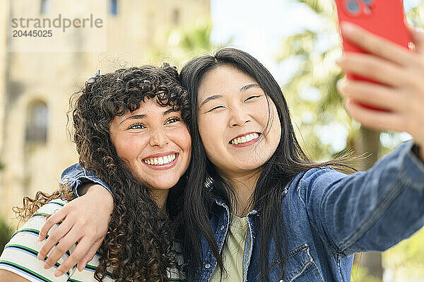 Smiling woman holding smartphone and taking selfie with friend