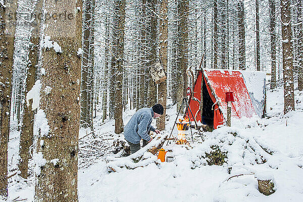 Senior man preparing campfire in snow near tent