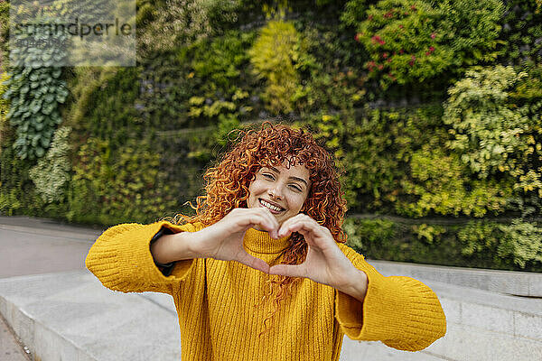 Smiling beautiful young redhead woman showing heart shape