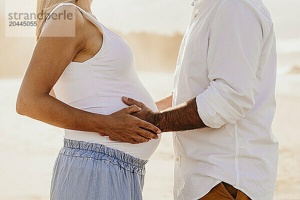 Man with hands on pregnant woman's stomach at beach