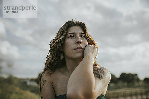 Thoughtful woman in front of cloudy sky