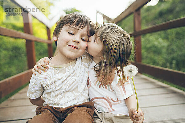 Girl kissing boy sitting on wooden bridge at park