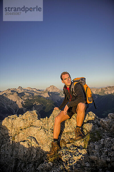 Young man sitting on Steinfeldspitze rock at sunrise in Altenmarkt  Zauchensee  Salzburg  Austria