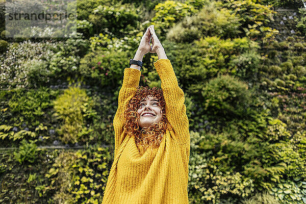 Smiling young woman with hands raised in front of green plants