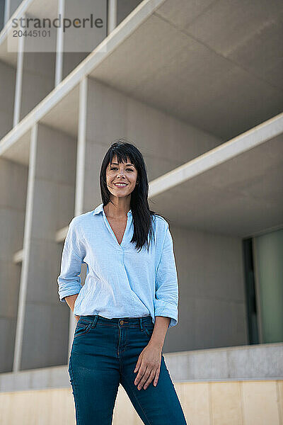 Smiling businesswoman with hand on hip in front of building