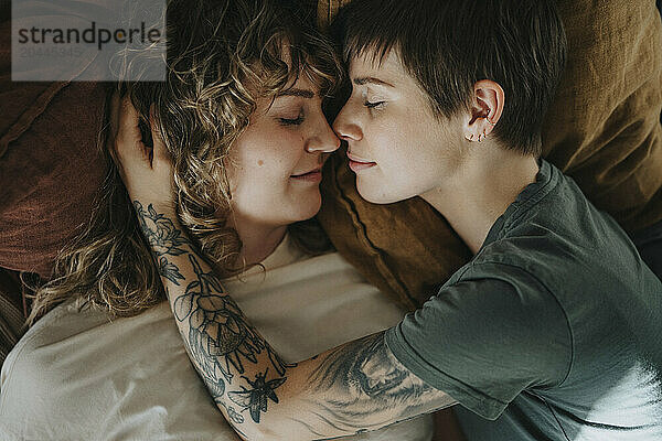 Directly above shot of lesbian couple rubbing noses while lying down on bed with eyes closed at home