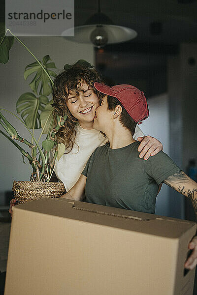 Lesbian woman carrying cardboard box kissing girlfriend during relocation