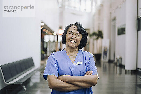 Portrait of smiling female doctor standing with arms crossed in hospital lobby