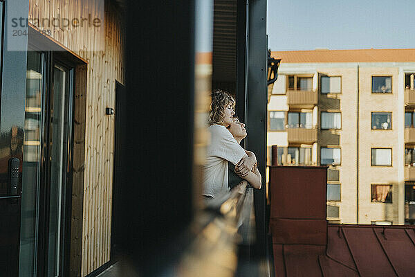 Romantic lesbian woman embracing girlfriend while standing with eyes closed in balcony