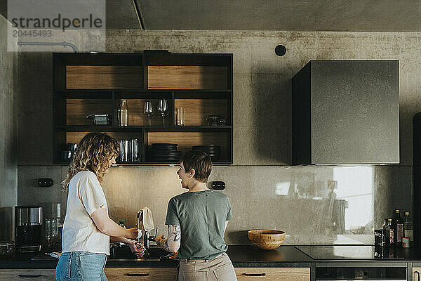 Happy lesbian couple washing dishes while standing in kitchen at home