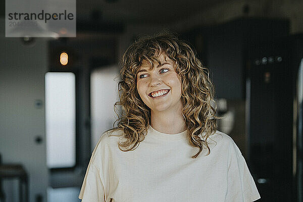 Smiling beautiful woman with curly hair looking away at home