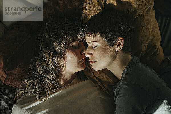 Directly above shot of lesbian couple lying face to face on bed at home