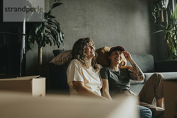 Happy lesbian couple having fun while sitting near sofa during relocation