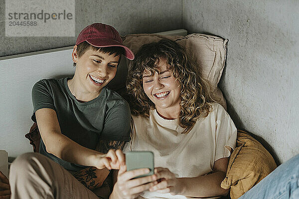 High angle view of happy lesbian couple having fun while using smart phone at home