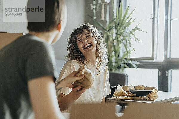 Happy lesbian woman with girlfriend wrapping utensil during relocation