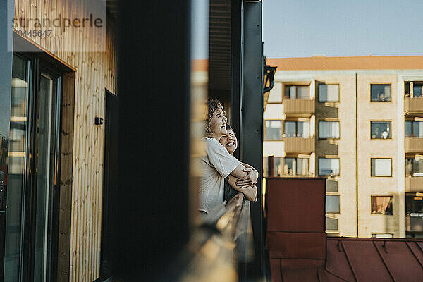 Happy lesbian woman embracing girlfriend while standing in balcony