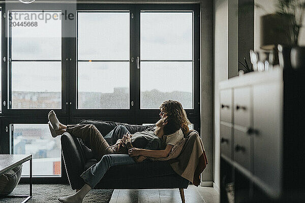 Lesbian couple lying together on sofa near window at home