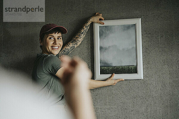 Smiling lesbian woman taking guidance from girlfriend while hanging frame on wall at home