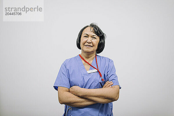 Portrait of confident female medical professional with arms crossed against white wall