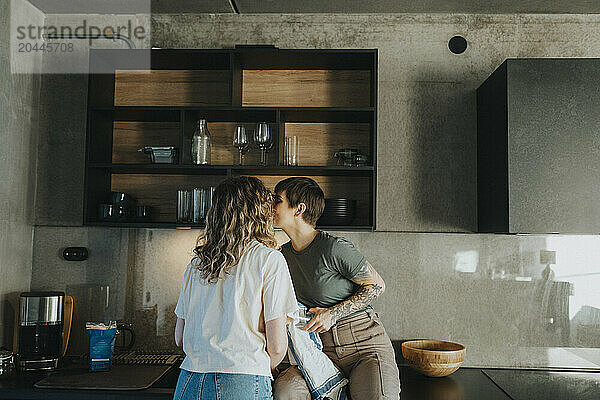 Lesbian woman sitting on kitchen counter kissing girlfriend at home