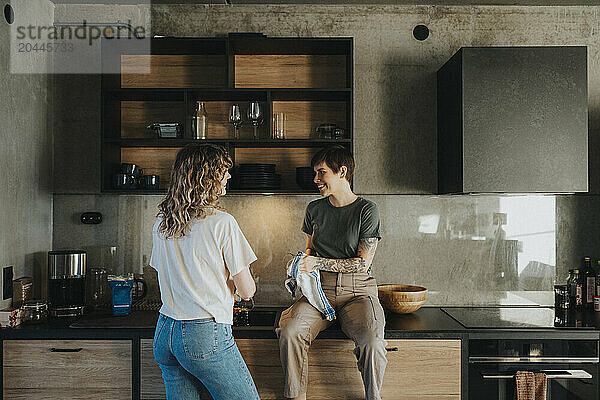 Lesbian woman helping girlfriend in cleaning dishes while sitting on kitchen counter at home