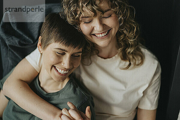 High angle view of happy lesbian woman with arm around girlfriend at home