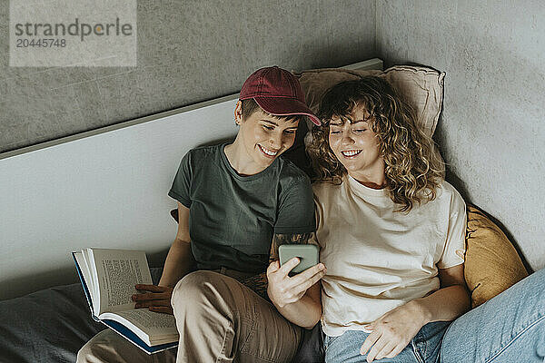 High angle view of happy lesbian couple using smart phone while lying on bed at home