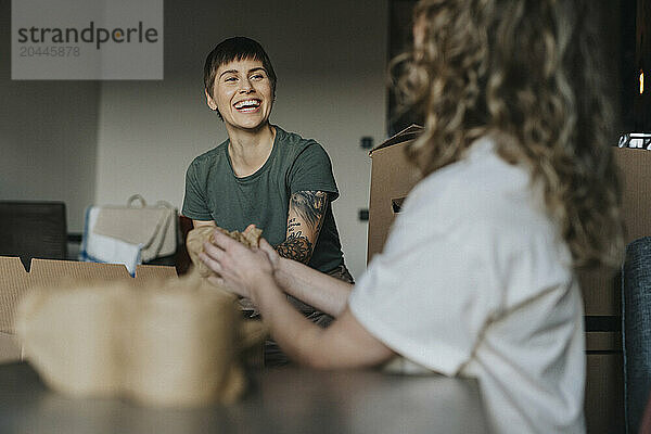 Happy lesbian woman sitting with girlfriend and wrapping stuff during relocation