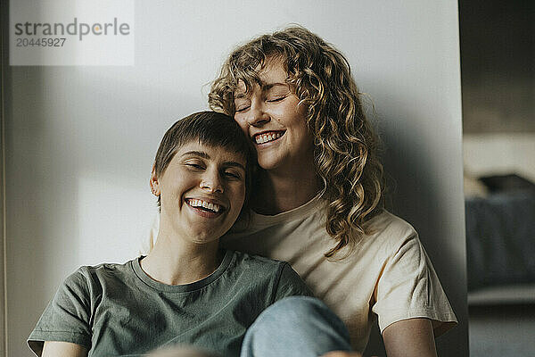 Happy lesbian couple sitting together near wall at home