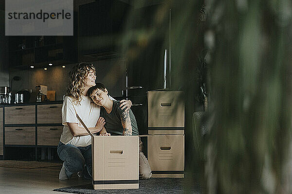 Lesbian woman embracing girlfriend packing stuff in cardboard box during relocation