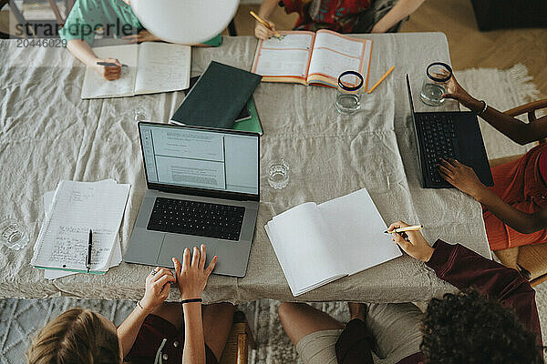 High angle view of group of friends doing homework and using laptop while sitting near table at home