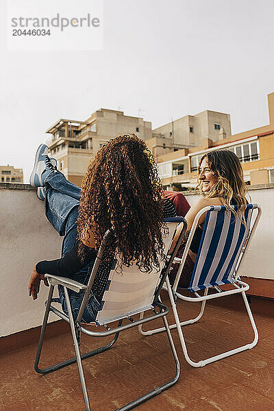 Smiling young woman sitting on chair next to female friend on rooftop