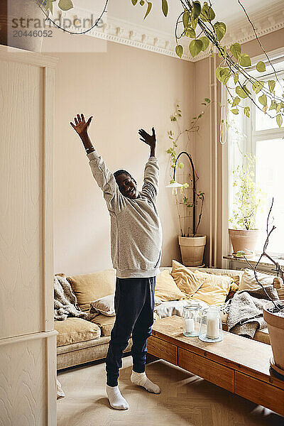 Teenage boy with arms raised standing in living room at home