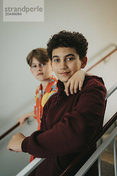 Portrait of boys moving down stairs with arm around at school