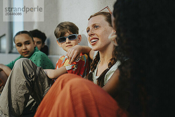 Thoughtful girl sitting with friends near wall