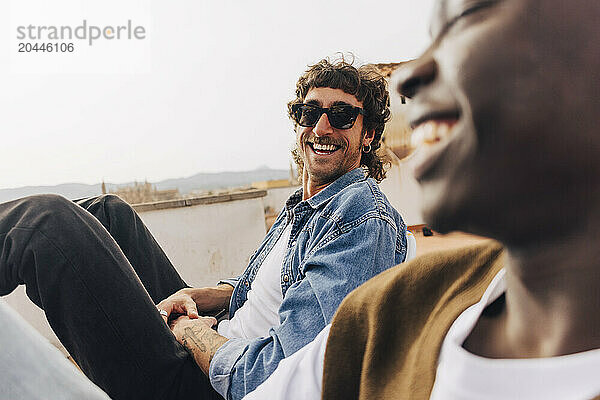 Smiling man sitting with male friend on building rooftop